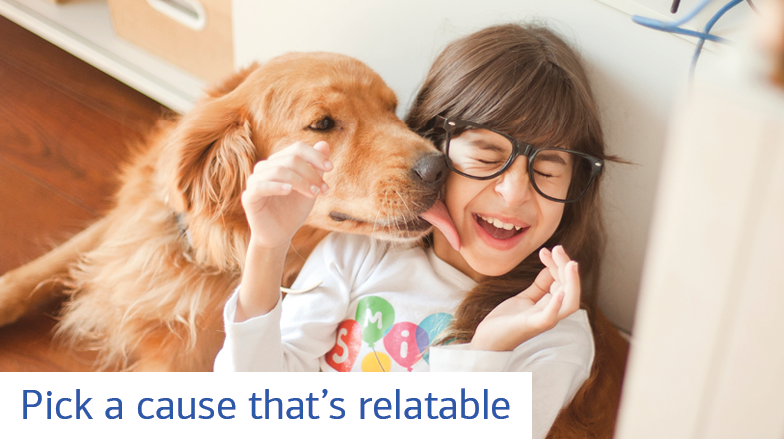 A young girl wearing glasses and sitting on the floor laughs as a dog licks her face. Text reads: Pick a cause that’s relatable