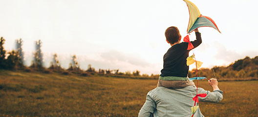 Young kid sitting on dad shoulder and holding kite