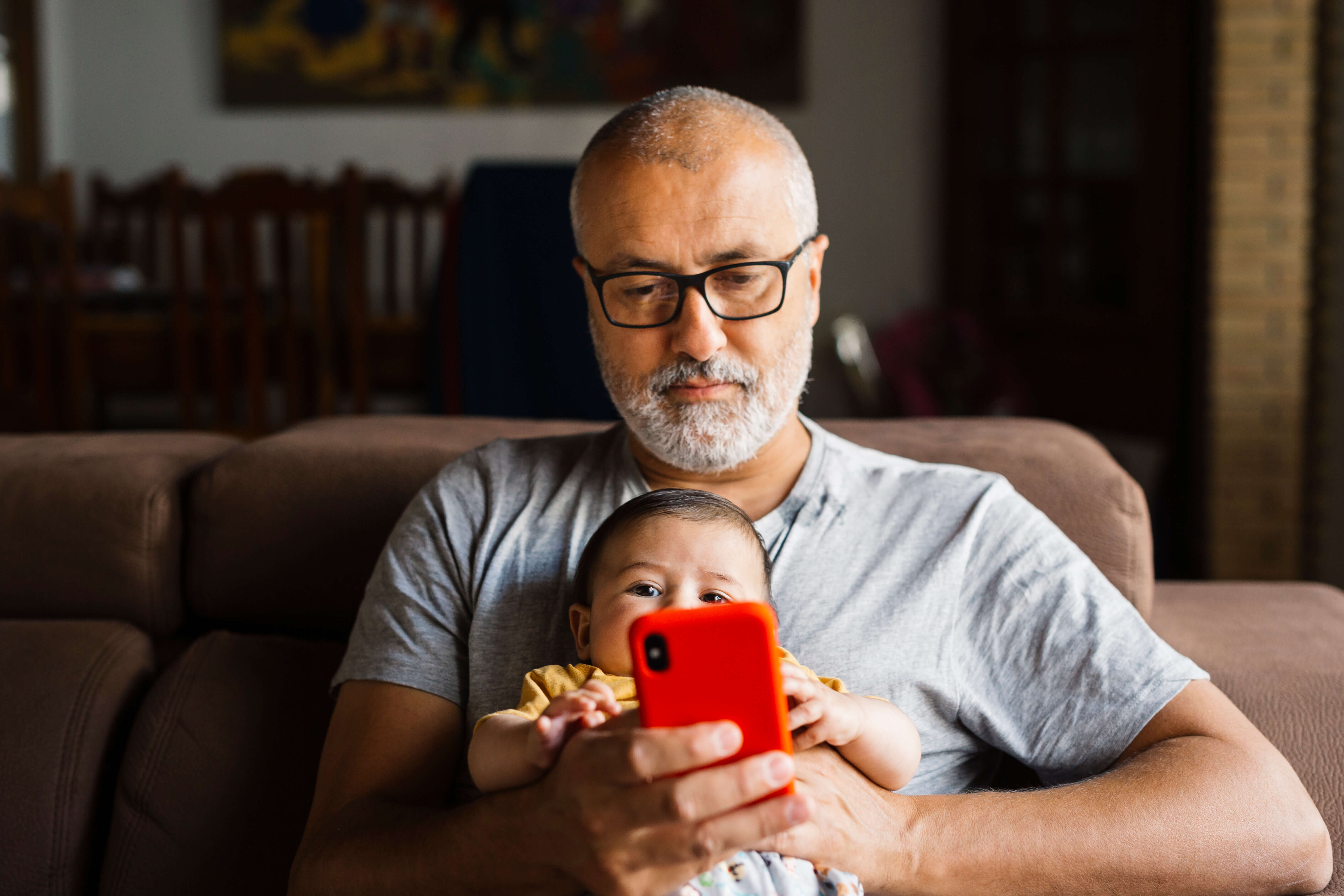 Middle age man holding a baby on his lap scrolling on a red smart phone